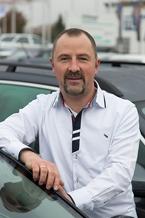 Ein Mitarbeiter steht vor einer geöffneten Tür eines Autos und schaut in die Kamera